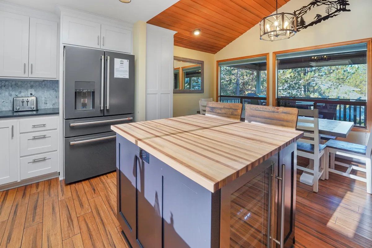 This image features a welcoming kitchen island with a view of the refrigerator and a bright dining area framed by large windows. The scene captures the heart of the home, where cooking and family meals naturally flow into one another, full of warmth and activity.