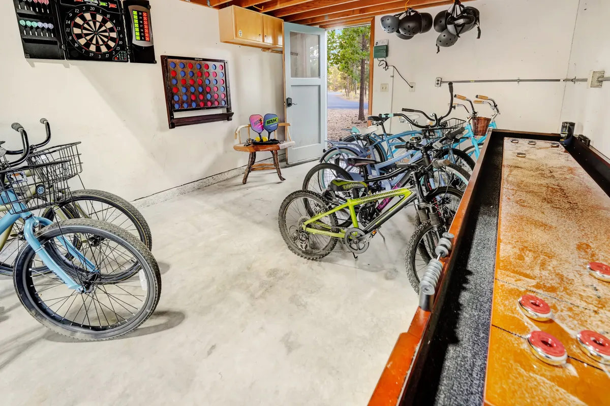 A lively garage transformed into a recreation room, featuring bikes ready for adventure, a dartboard, and a game table. The open garage door hints at easy access to outdoor activities and communal fun.