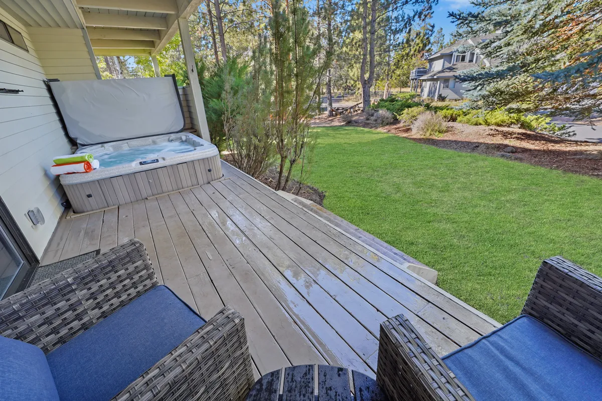 This exterior image captures a hot tub nestled within a tranquil deck setting, surrounded by a lush green lawn and mature trees. The outdoor seating area invites relaxation and gatherings, while the view emphasizes a seamless connection to Sunriver’s nature. The hot tub is professionally maintained and positioned to offer privacy and views of the native landscaping.