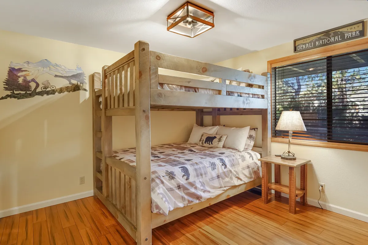 A family-friendly bunk room with a queen-over-queen bunk bed, playful wall mural, and a soft table lamp. The room radiates a sense of adventure and comfort, perfect for families or friends. The cozy bedding and whimsical decor invite relaxation and fun.