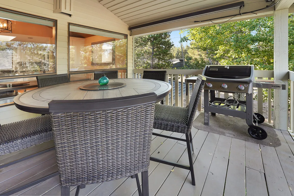 An outdoor dining area with a round table, barbecue grill, and vibrant decorative accents, set against a backdrop of greenery. The scene suggests opportunities for outdoor meals, social gatherings, and casual fun for both people and pets.