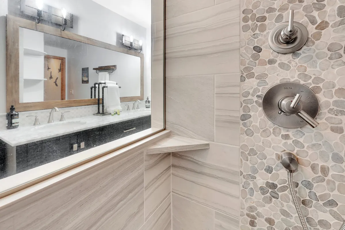 A contemporary bathroom with pebble tile walls and modern shower fixtures, complemented by a spacious vanity and large mirror. The space is tranquil and spa-like, ideal for unwinding after a day of adventure.