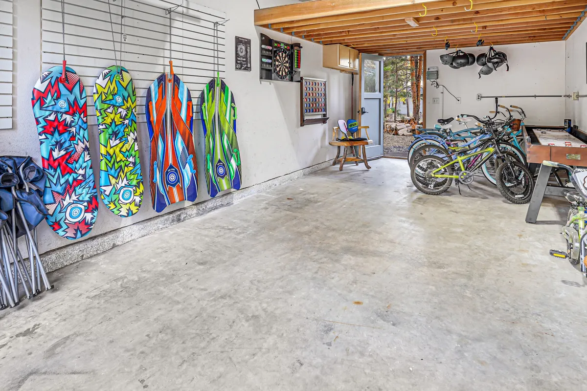 A vibrant garage activity space showcasing colorful snowboards, a row of bicycles in various sizes, and a dartboard mounted on the wall. Natural light streams in, making the space feel energetic and inviting—a true hub for active fun and games regardless of the weather.