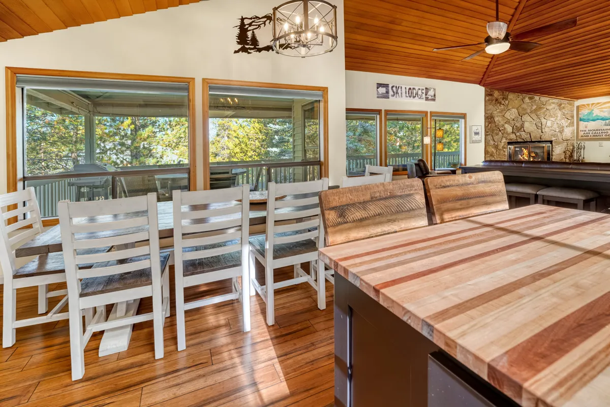A spacious dining area with a large table, wooden counters, a stone fireplace, and expansive windows. The room is set for gathering, with cozy yet elegant touches perfect for shared meals and celebrations.
