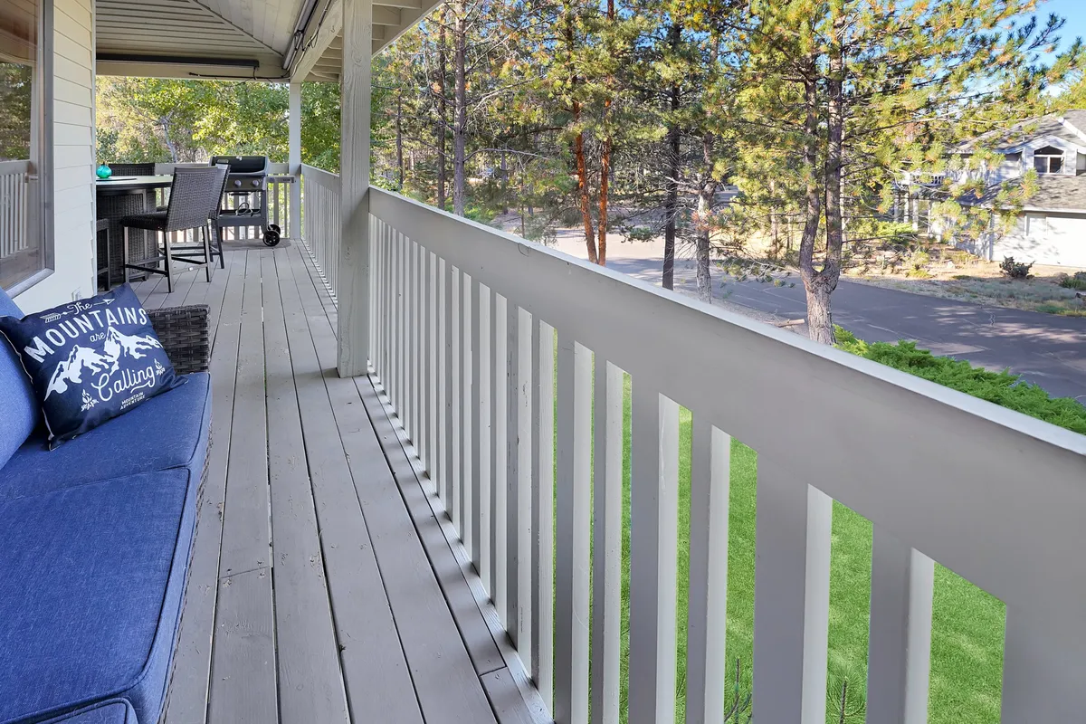 An inviting outdoor space featuring a blue outdoor couch, dining table, and a lush green lawn bordered by tall trees. The setup encourages gatherings, relaxation, and enjoying the natural surroundings.