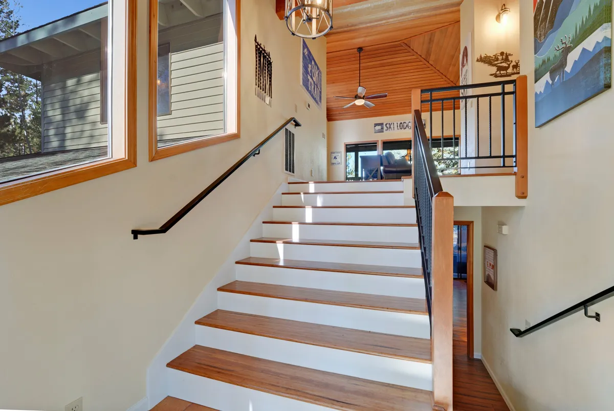 The image captures the home's entryway with a graceful staircase, large windows flooding the space with natural light, and tasteful wall art. The space feels welcoming and airy, hinting at the inviting atmosphere awaiting groups arriving for a memorable stay.